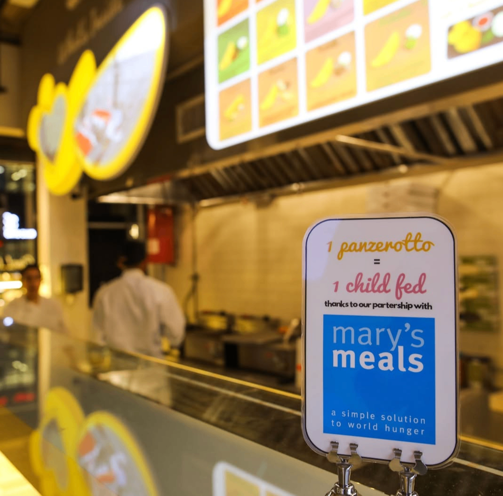 Cartello “1 panzerotto = 1 child fed” in partnership con Mary's Meals esposto al bancone di un nostro store
