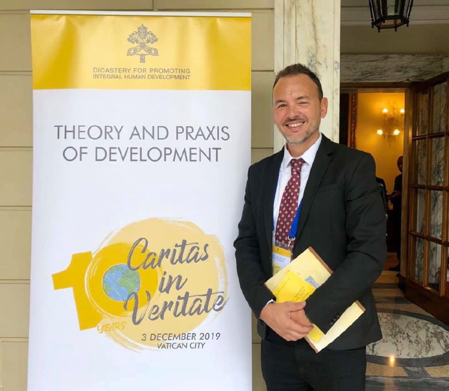 Angelo Magni davanti al banner della conferenza Caritas in Veritate, Città del Vaticano, 3 dicembre 2019
